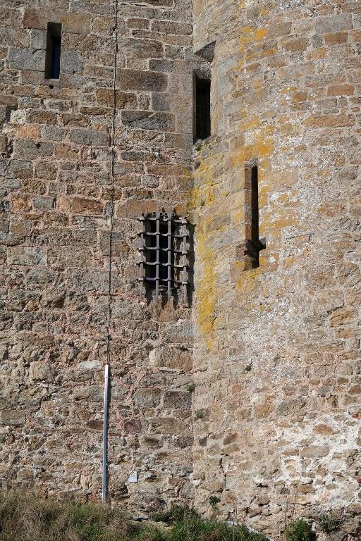 Vue de détail de l'élévation sud de la tour. Au rez-de-chaussée : jour grillée de la cage descalier et arbalétrière-canonnière de la tour est (dépourvue d'arc de décharge). En haut,  jours/arbalétrières de la cage descalier au niveau intermédiaire