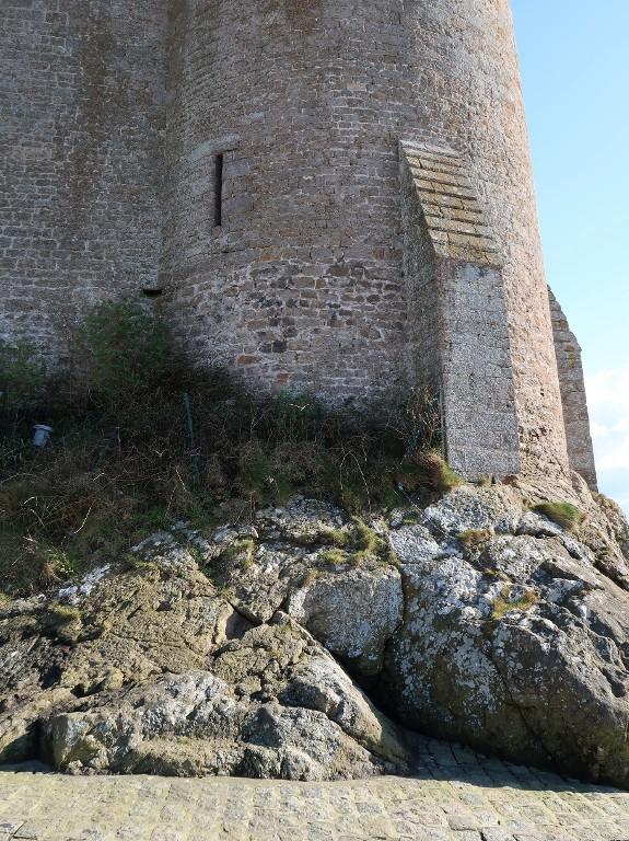 Vue du pied de la tour ouest depuis le nord : deux mises en oeuvre différentes sont visibles dans la maçonnerie. En haut, au centre, archère-canonnière (dépourvue d'arc de décharge) du rez-de-chaussée ; à droite, contrefort nord en pierre de taille